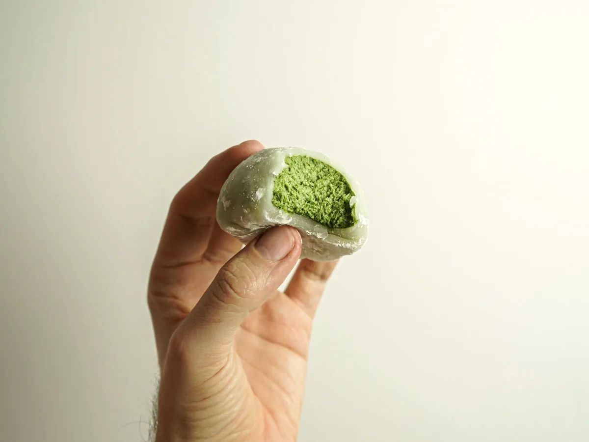 半分に割った緑の菓子を手で持ち、中の餡を見せているところ
