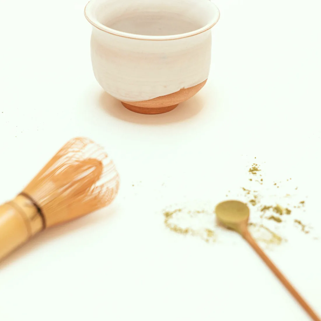 白い机に置かれた茶碗と茶筅、こぼれた抹茶と茶杓