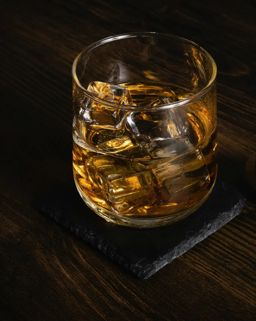 濃い木のカウンターに置かれた、氷の大きい琥珀の一杯