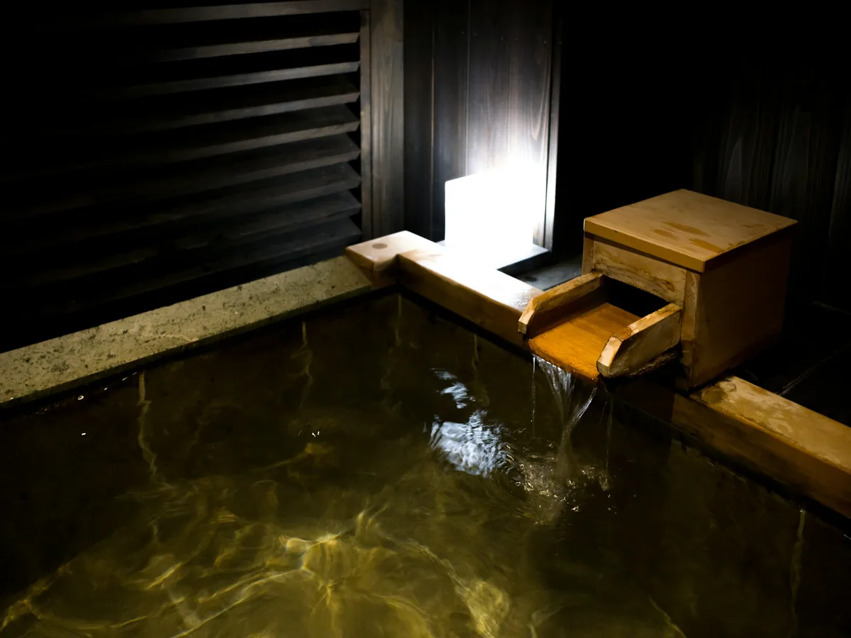 灯りをひとつだけ落とした湯殿と、木の湯口から落ちる湯
