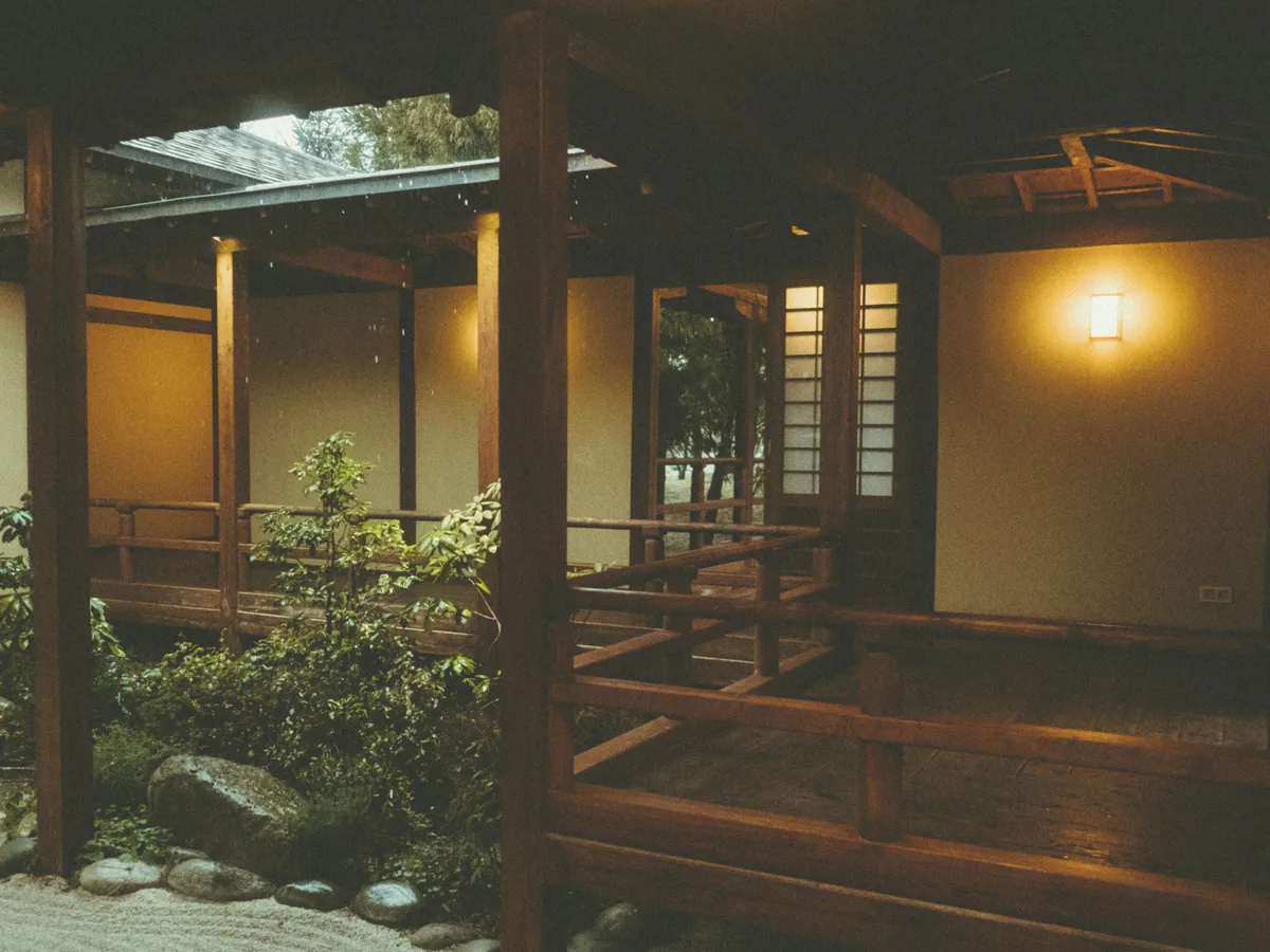 夕方の広縁。木の欄干の向こうに坪庭、壁に灯りがひとつ