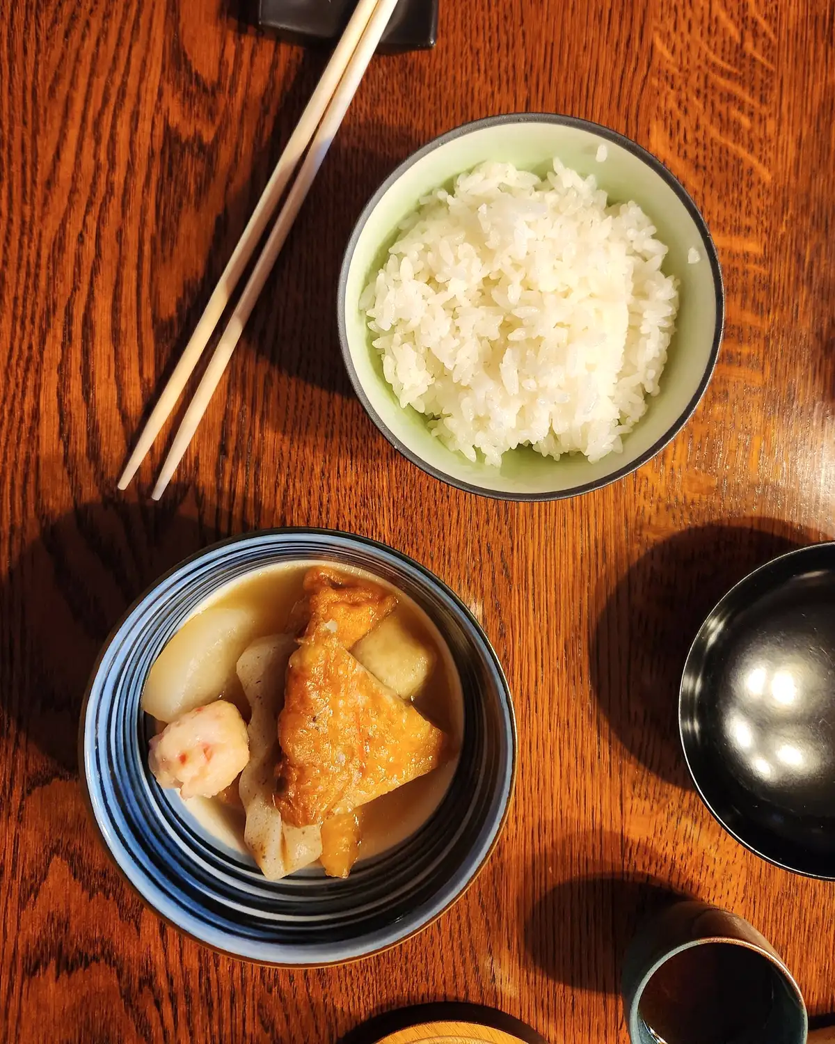 濃い木のテーブルに置かれた白いごはんの椀と、揚げ出し豆腐と大根の小鉢